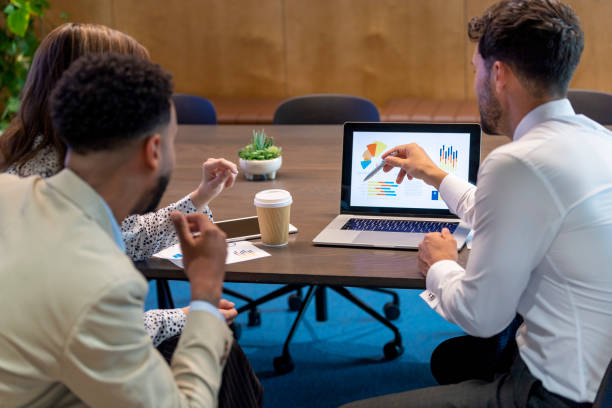 Financial advisor or lawyer with couple explaining options. They are discussing finance charts and graphs on a laptop computer. They sitting in an office and are discussing something with the agent